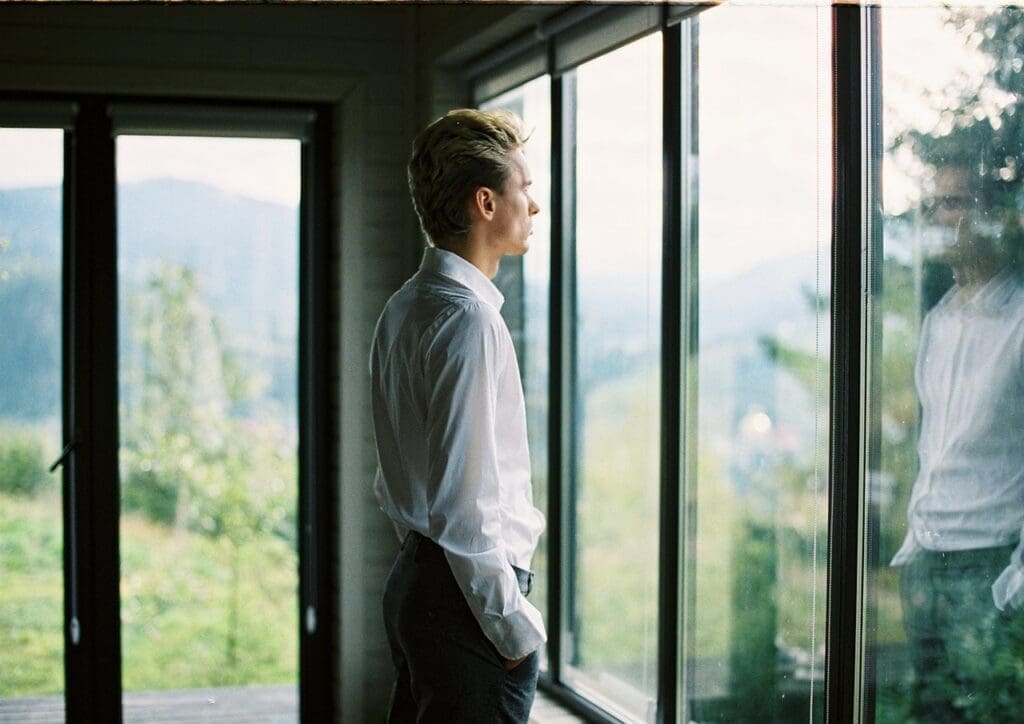 Calm well dressed male standing near window at home